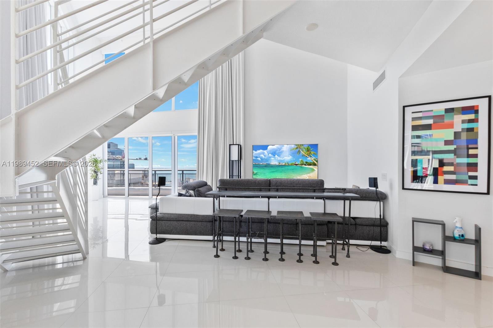 A modern living room features a white staircase, tiled floors, and a balcony with views — 60 SW 13th St # 3800, Miami FL 33130, MIAMI, FL