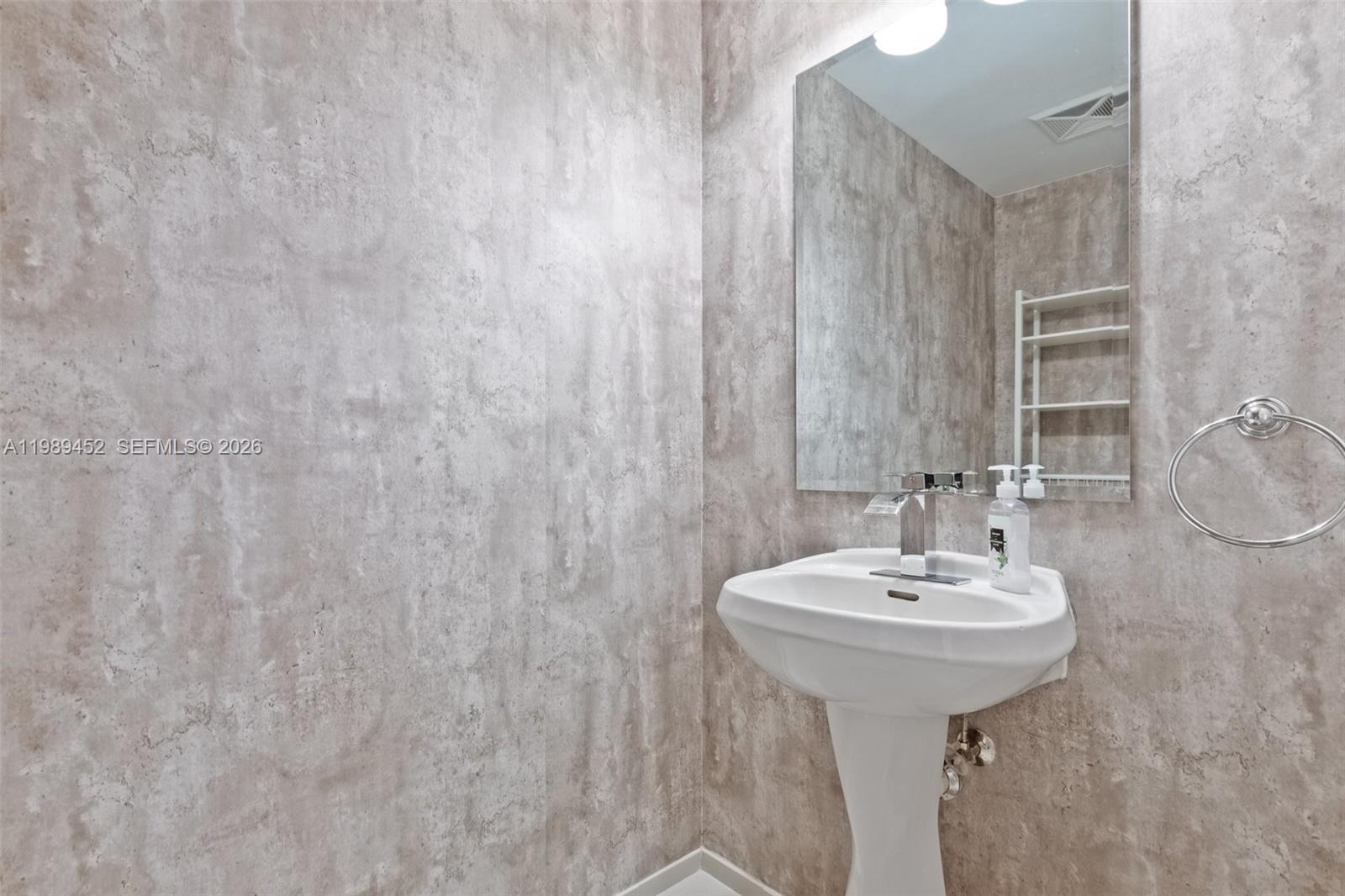 A bathroom features a pedestal sink, a wall-mounted mirror, and textured gray wall panels — 60 SW 13th St # 3800, Miami FL 33130, MIAMI, FL