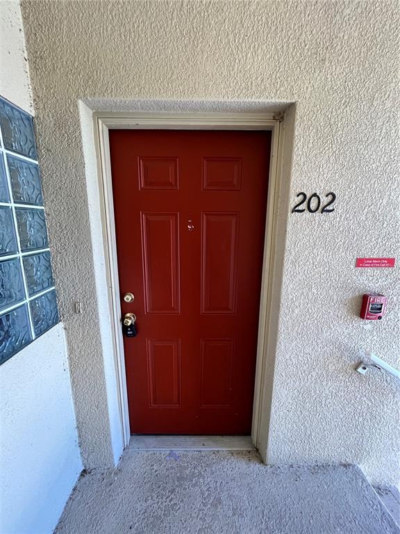 A red front door with the number 202 is set into a textured beige exterior wall — 6456 CYPRESSDALE DRIVE UNIT 202, RIVERVIEW, FL