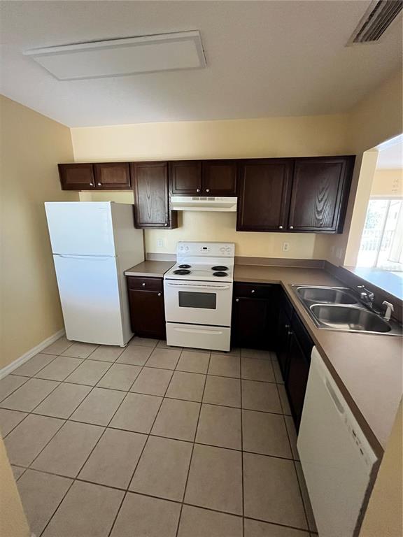 A kitchen features dark wood cabinets, white appliances, tan countertops, and light-colored tile flooring — 6456 CYPRESSDALE DRIVE UNIT 202, RIVERVIEW, FL