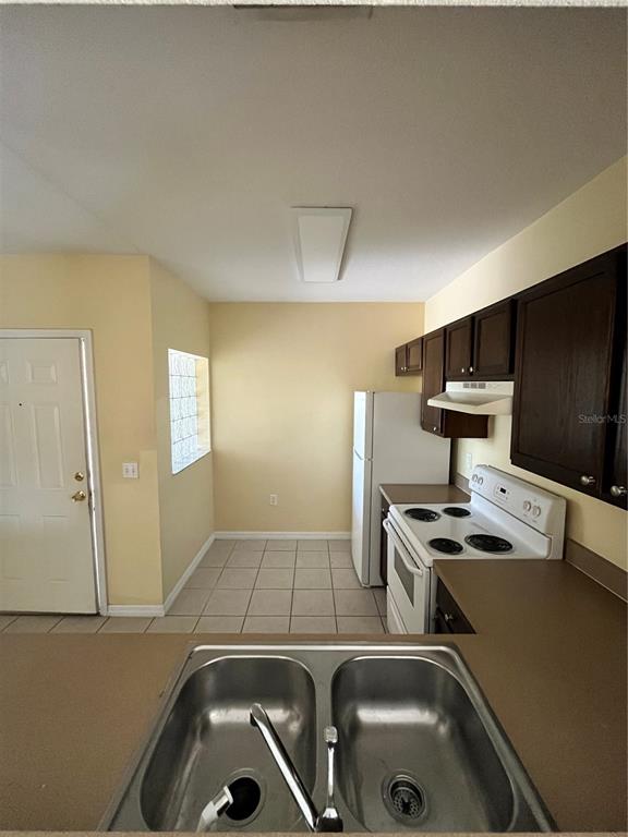 A kitchen features a double-basin sink, white appliances, dark wood cabinets, and tile flooring — 6456 CYPRESSDALE DRIVE UNIT 202, RIVERVIEW, FL