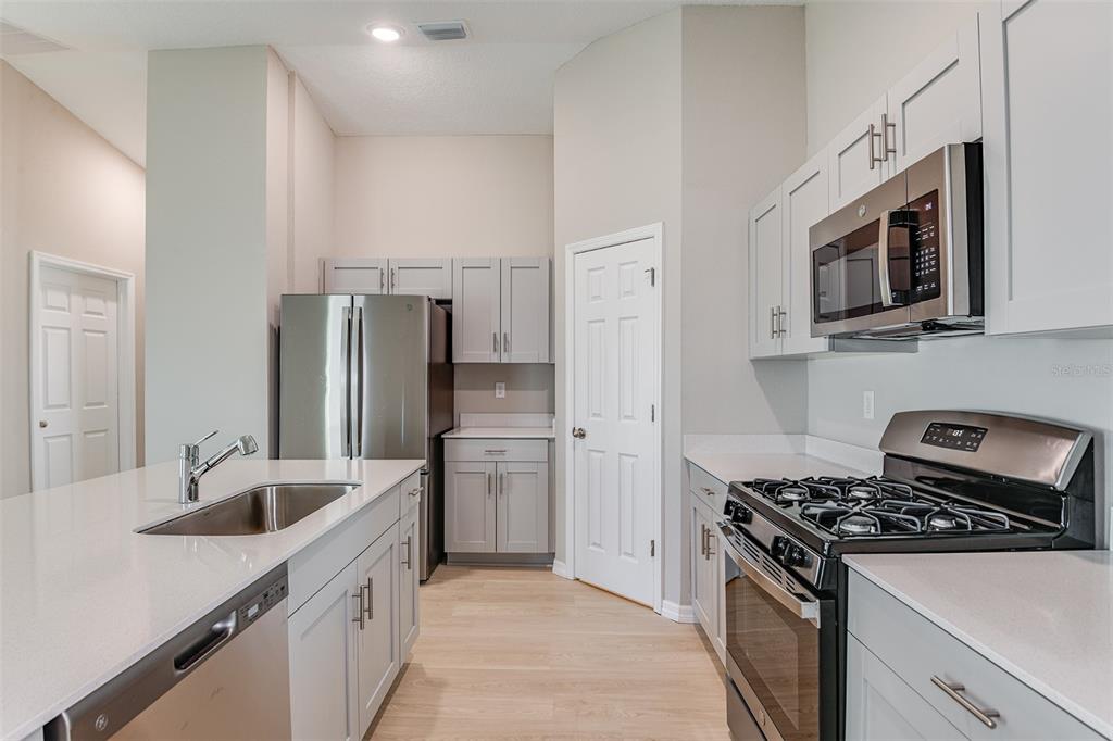 A modern kitchen features light gray cabinets, stainless steel appliances, and a white quartz island — 6056 NAVONA WAY, WINTER HAVEN, FL