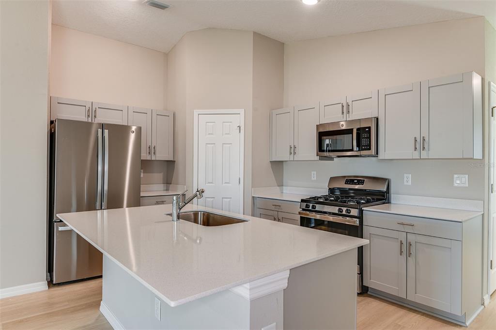 A kitchen with light gray cabinets, stainless steel appliances, and a central island with quartz countertops — 6056 NAVONA WAY, WINTER HAVEN, FL