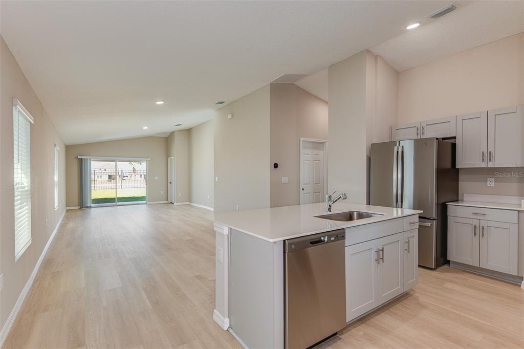 A kitchen with light gray cabinets and stainless steel appliances overlooks an open living area — 6056 NAVONA WAY, WINTER HAVEN, FL