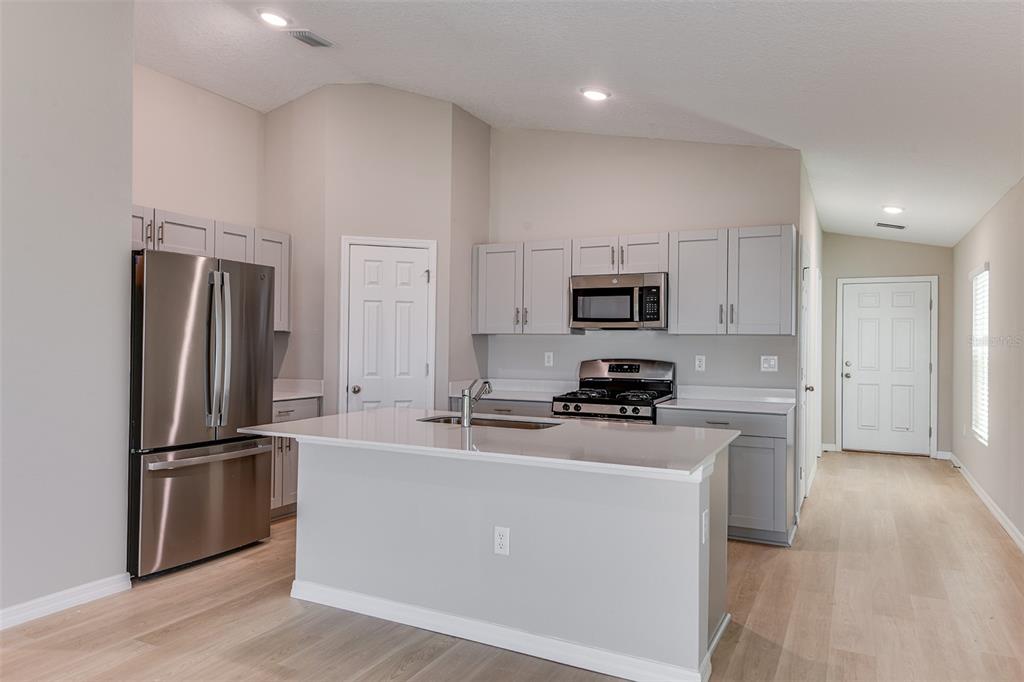 A modern kitchen features light gray cabinets, stainless steel appliances, and a central island — 6056 NAVONA WAY, WINTER HAVEN, FL