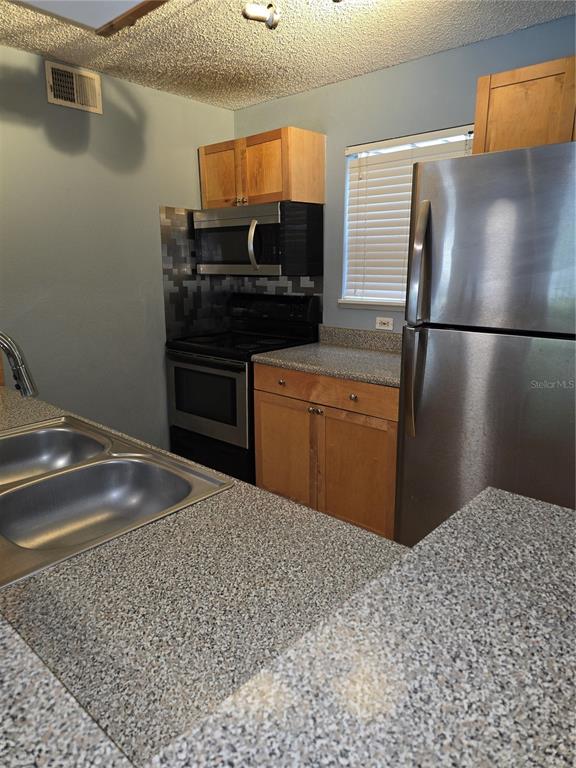A kitchen features light wood cabinets, granite-look countertops, stainless steel appliances, and a double sink — 2500 WINDING CREEK BOULEVARD UNIT E205, CLEARWATER, FL