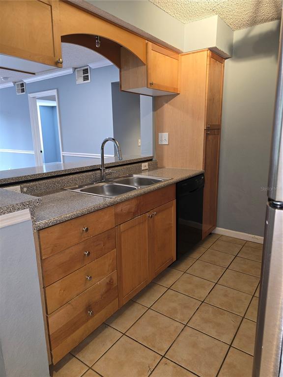 A kitchen features light wood cabinets, granite countertops, a double sink, and beige tile flooring — 2500 WINDING CREEK BOULEVARD UNIT E205, CLEARWATER, FL