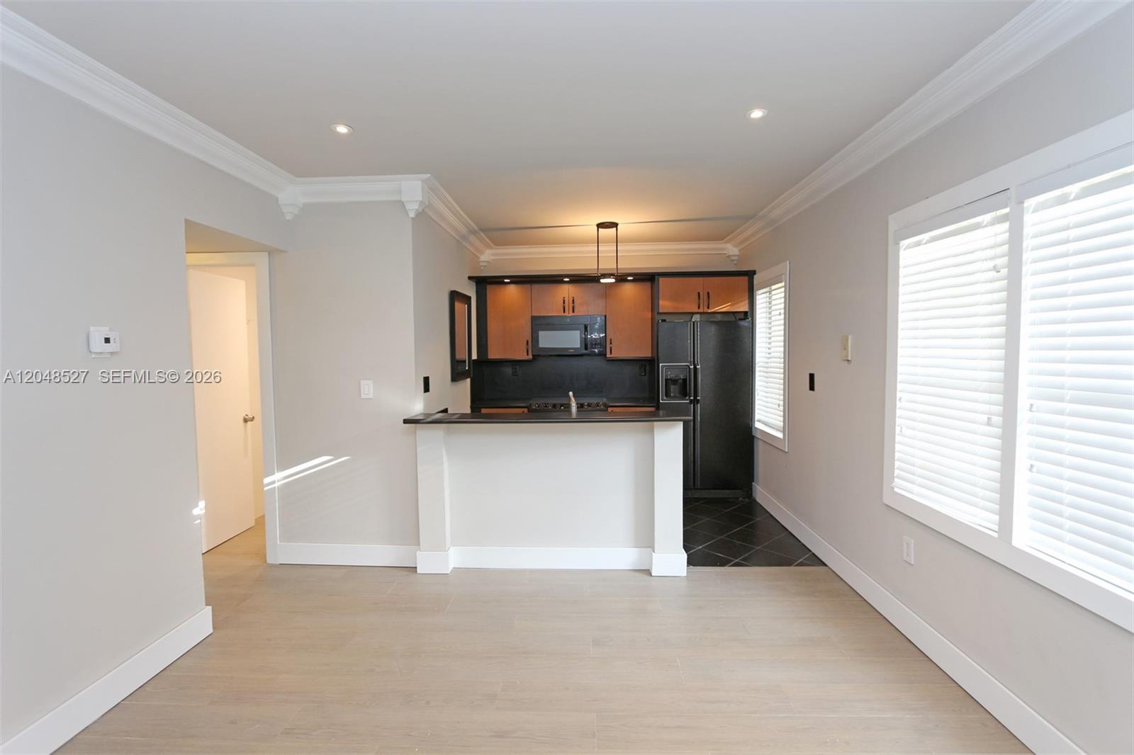 A kitchen features a breakfast bar, dark cabinetry, black appliances, and light wood-look flooring — 3395 Franklin Ave # D, Miami FL 33133, MIAMI, FL