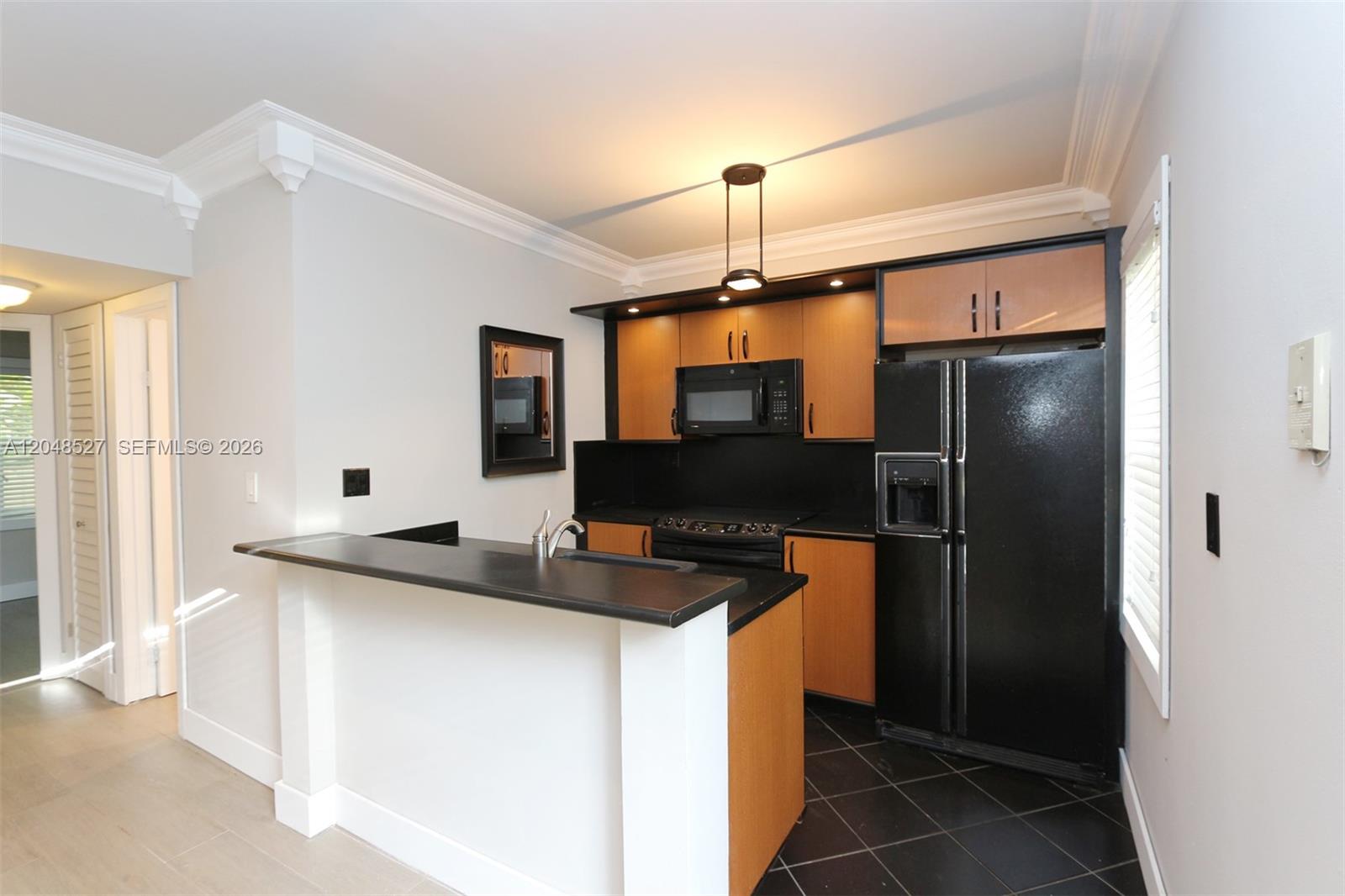 A kitchen features wood cabinets, black appliances, a breakfast bar, and dark tile flooring — 3395 Franklin Ave # D, Miami FL 33133, MIAMI, FL