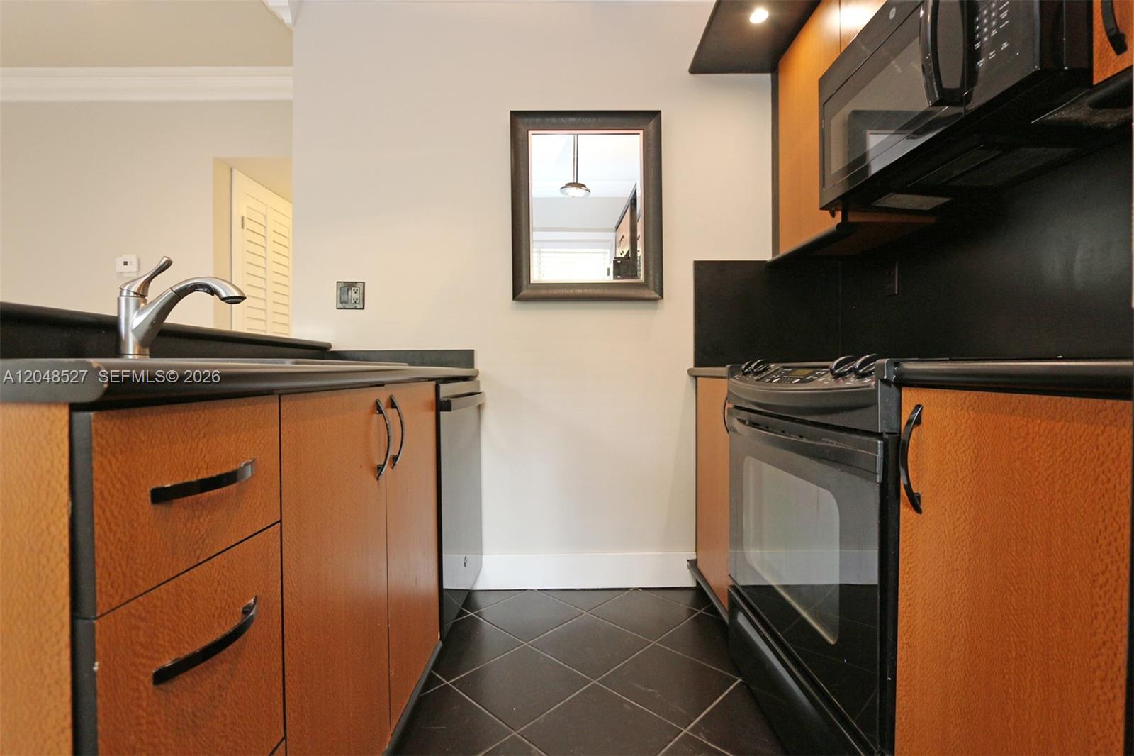 A galley kitchen features wood-grain cabinets, black countertops, a black stove, and dark tile flooring — 3395 Franklin Ave # D, Miami FL 33133, MIAMI, FL