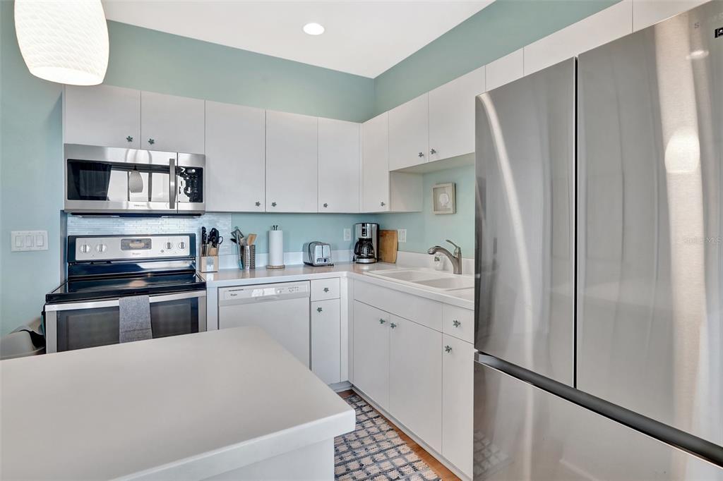 A kitchen features white cabinetry, stainless steel appliances, light countertops, and light blue walls — 2090 MATECUMBE KEY ROAD UNIT 1708, PUNTA GORDA, FL