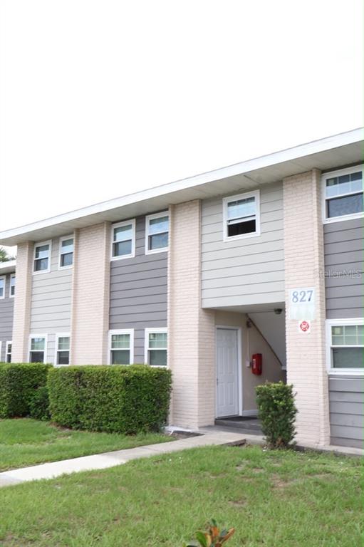 A two-story apartment building exterior features light-colored brick columns, gray siding, and green hedges — 827 SKY LAKE CIRCLE UNIT A, ORLANDO, FL