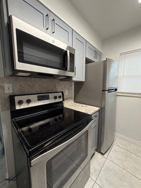 A kitchen features stainless steel appliances, gray cabinets, granite countertops, and a herringbone tile backsplash — 827 SKY LAKE CIRCLE UNIT A, ORLANDO, FL