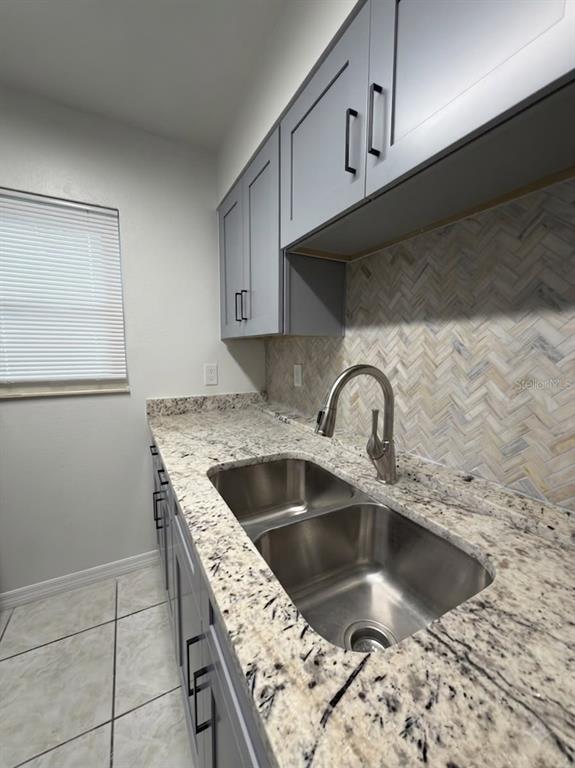 A kitchen features gray cabinets, granite countertops, a stainless steel sink, and a herringbone backsplash — 827 SKY LAKE CIRCLE UNIT A, ORLANDO, FL