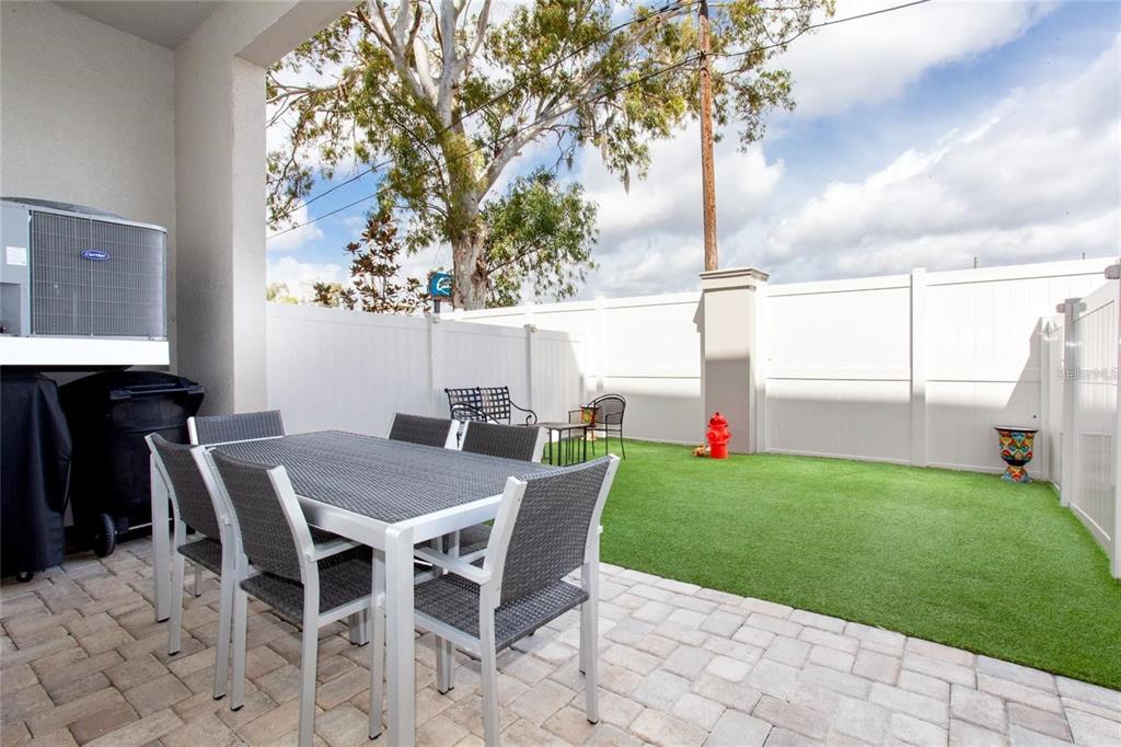 A patio with a dining set and artificial turf yard enclosed by a white fence — 1273 SAVONA DRIVE NE, ST PETERSBURG, FL