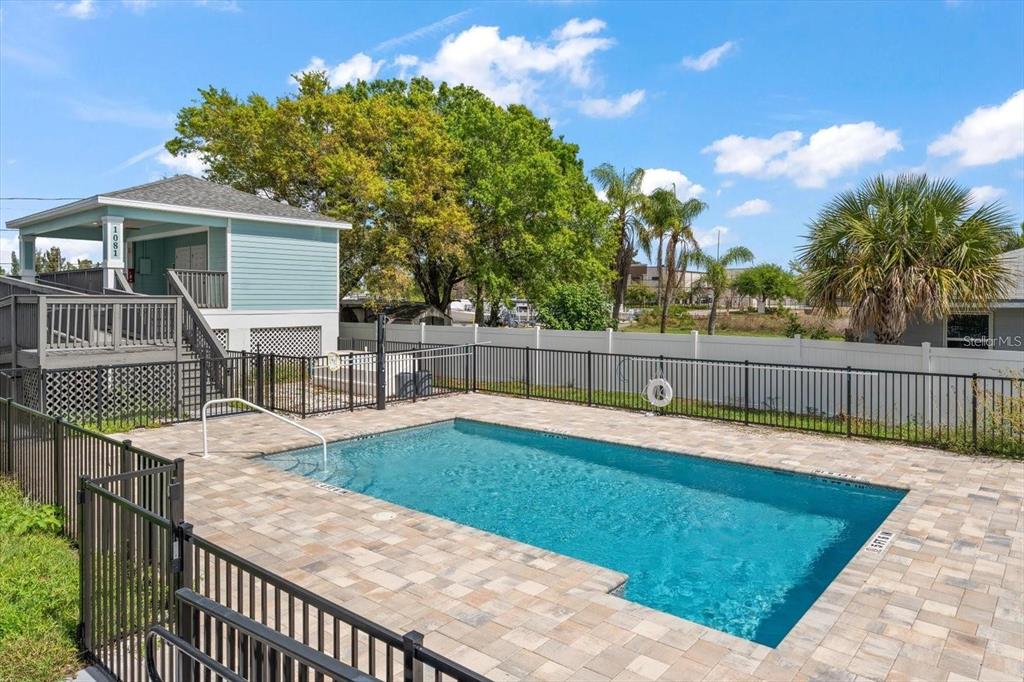 A rectangular swimming pool with a paver deck sits beside a raised house with stairs — 1273 SAVONA DRIVE NE, ST PETERSBURG, FL