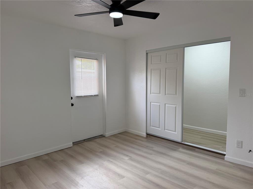 A bedroom features light wood-look flooring, a ceiling fan, a white door, and a mirrored closet — 10909 N 14TH STREET, TAMPA, FL