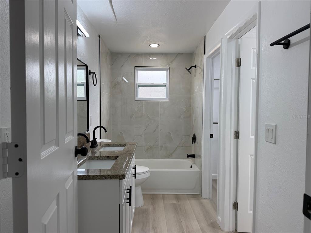 A bathroom features a double vanity, a tiled tub-shower combination, and light wood-look flooring — 10909 N 14TH STREET, TAMPA, FL