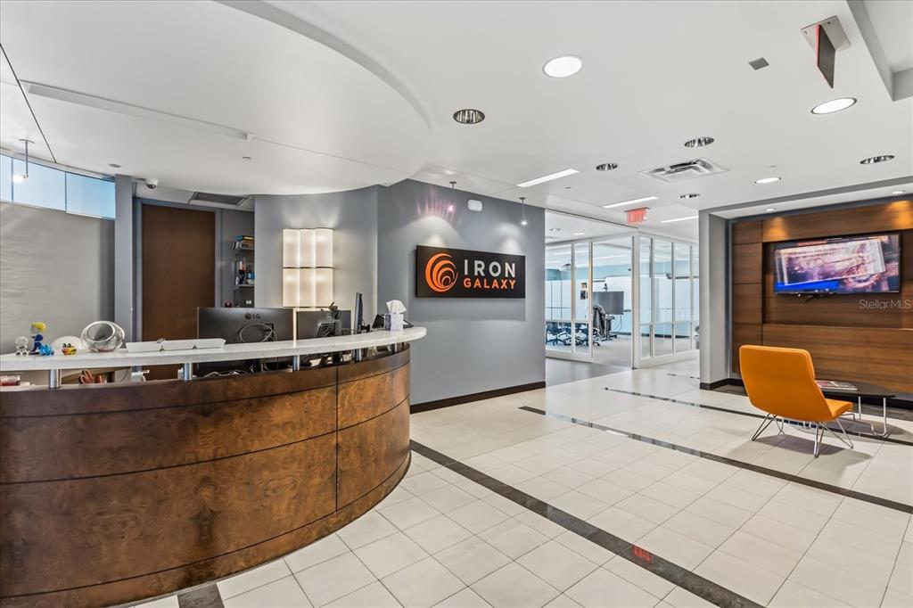 A modern office reception area features a curved wood desk, tile flooring, and company signage — 189 S ORANGE AVENUE UNIT 1900-1970, ORLANDO, FL