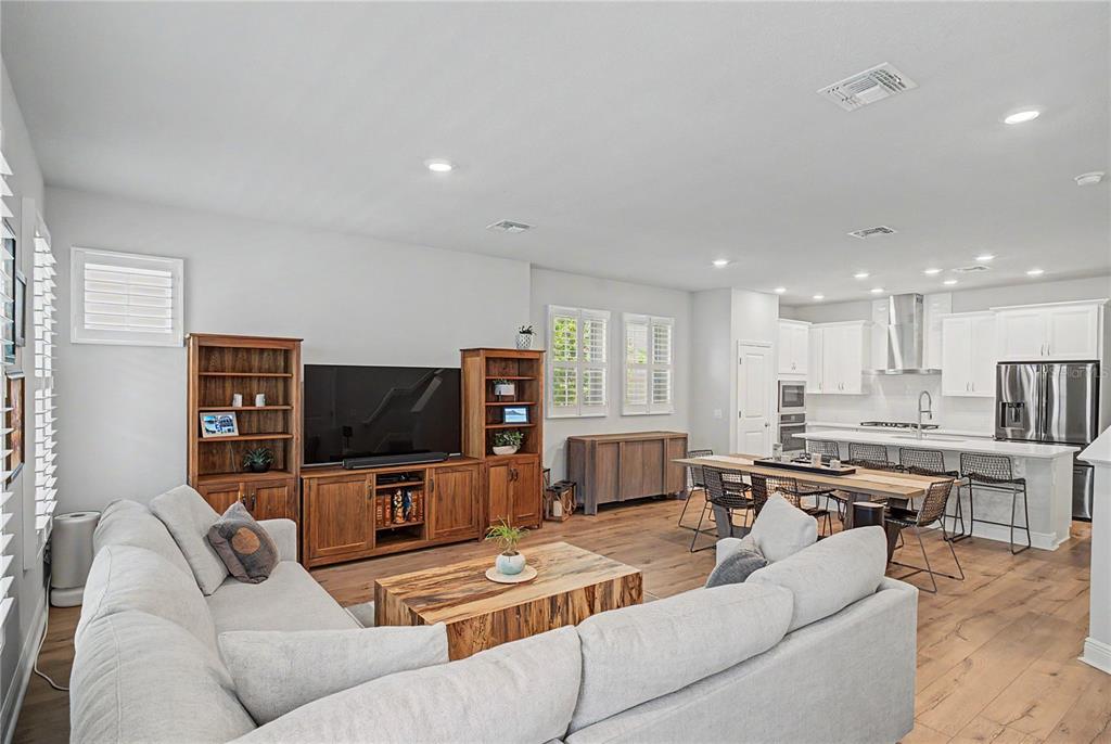 An open-concept living room features a sectional sofa, wooden media console, and adjacent kitchen area — 914 TROWMAN ALLEY, WINTER GARDEN, FL
