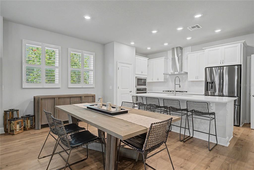 A modern kitchen and dining area feature white cabinetry, a large island, and wood flooring — 914 TROWMAN ALLEY, WINTER GARDEN, FL
