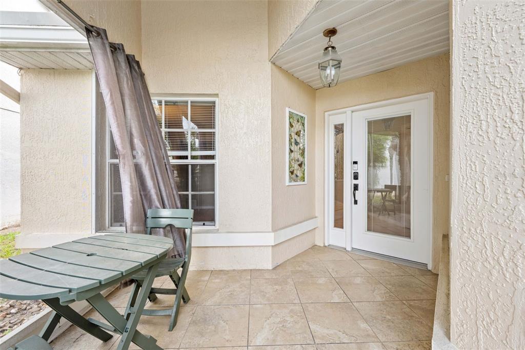 A covered patio features tiled flooring, a small table with a chair, and a front door — 9354 MISSISSIPPI RUN, WEEKI WACHEE, FL