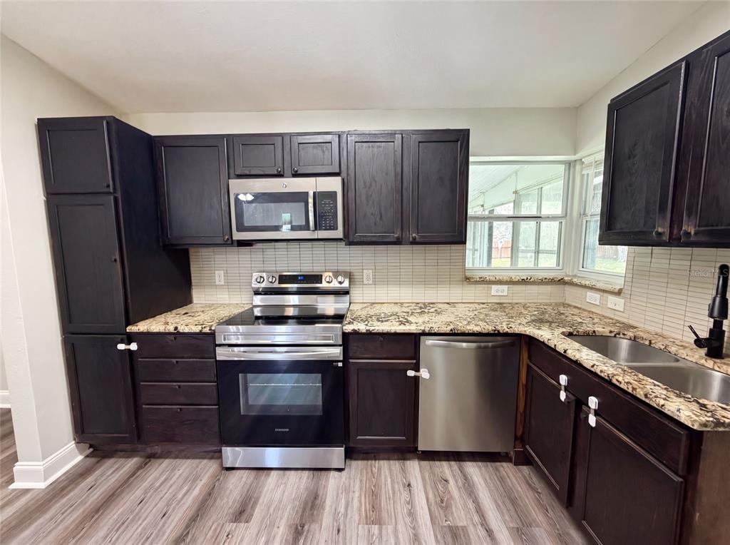 A kitchen features dark wood cabinets, granite countertops, stainless steel appliances, and light wood flooring — 1502 DAROCA DRIVE, DELTONA, FL
