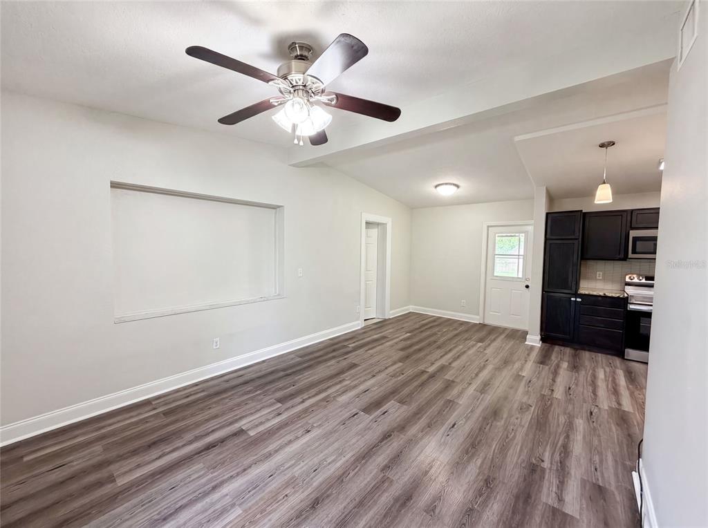 An open-concept living area features wood-look flooring, a ceiling fan, and an adjacent kitchen — 1502 DAROCA DRIVE, DELTONA, FL