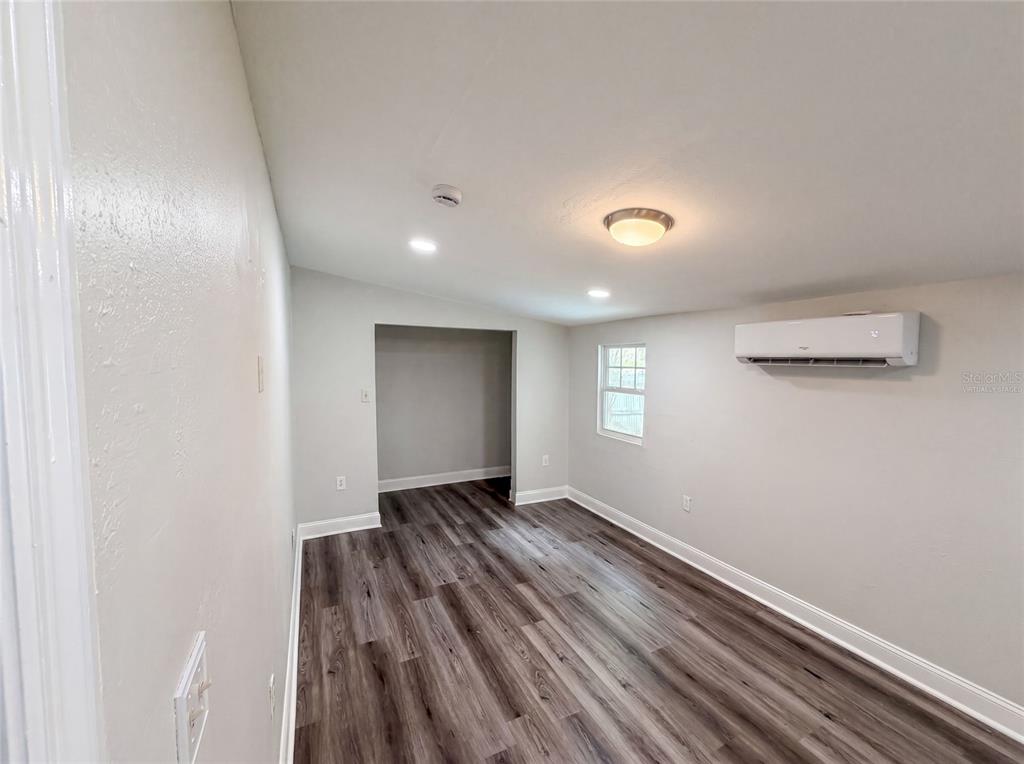 A room with wood-look flooring, light gray walls, a window, and a wall-mounted air conditioner — 1502 DAROCA DRIVE, DELTONA, FL