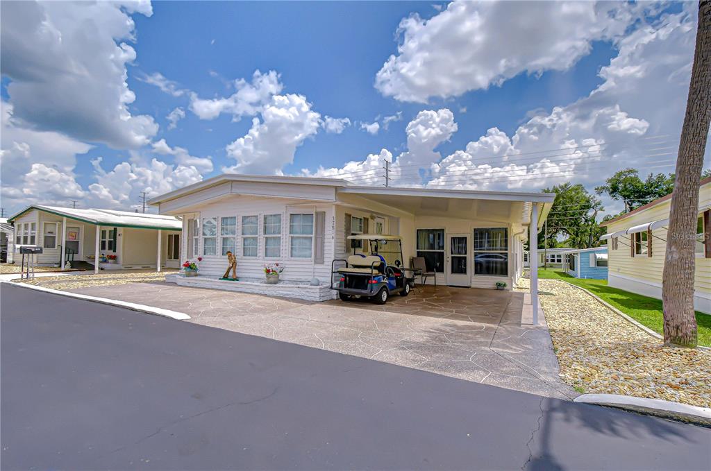 A white mobile home features a paved carport, a golf cart, and a stone-textured driveway — 37816 BARCELONA AVENUE, ZEPHYRHILLS, FL