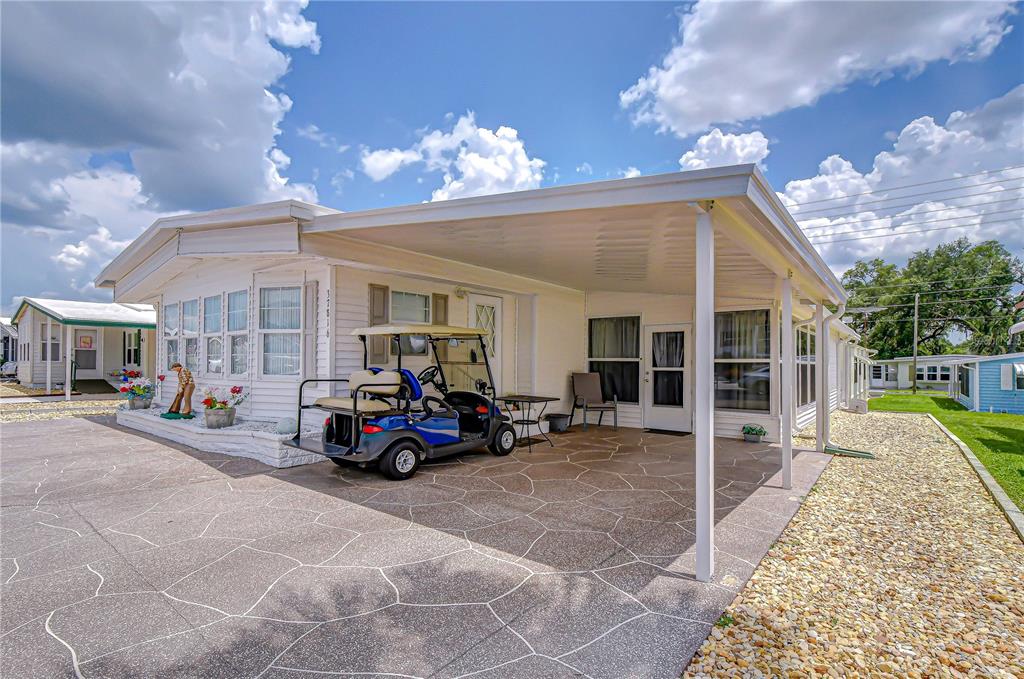 A white mobile home features a covered carport, a golf cart, and a patterned driveway — 37816 BARCELONA AVENUE, ZEPHYRHILLS, FL