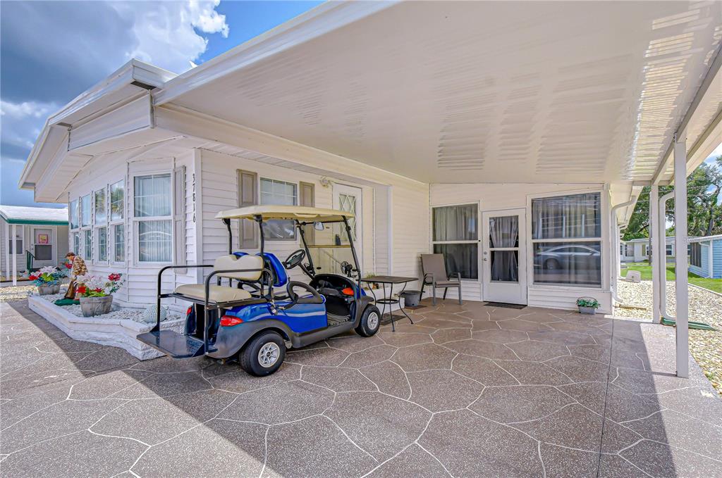 A blue golf cart sits on a patterned concrete patio under a covered carport — 37816 BARCELONA AVENUE, ZEPHYRHILLS, FL
