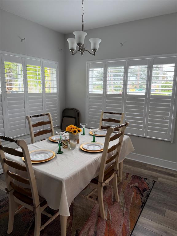 A dining room features a table set for four, white plantation shutters, and a chandelier — 20705 MOUNTAIN WHISTLER AVENUE, VENICE, FL