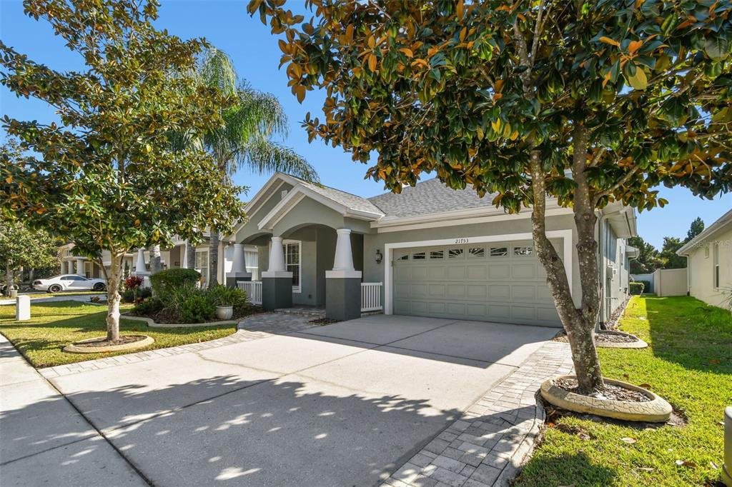 A single-story house with a two-car garage, a covered entryway, and mature trees in front — 21753 GARDEN WALK LOOP, LAND O LAKES, FL