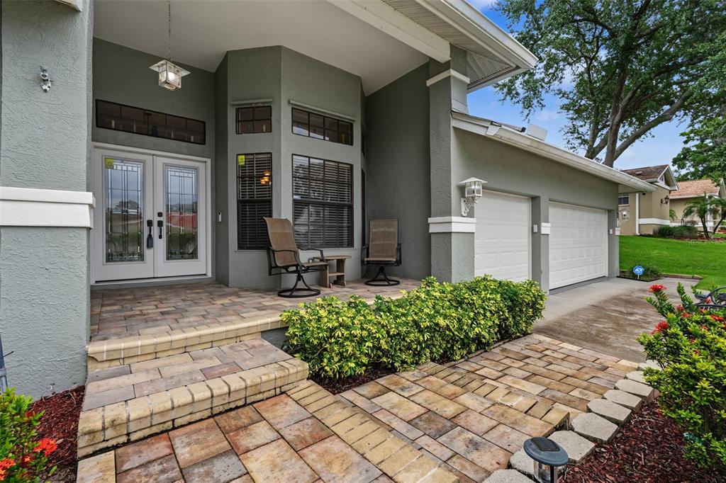 A gray house exterior features a paver walkway, a covered porch, and a two-car garage — 605 TOMOKA DRIVE, PALM HARBOR, FL