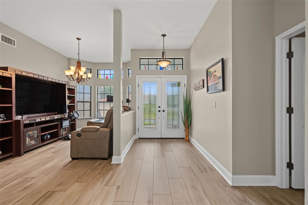 A foyer with light wood-look tile flooring leads to a living area with double doors — 605 TOMOKA DRIVE, PALM HARBOR, FL