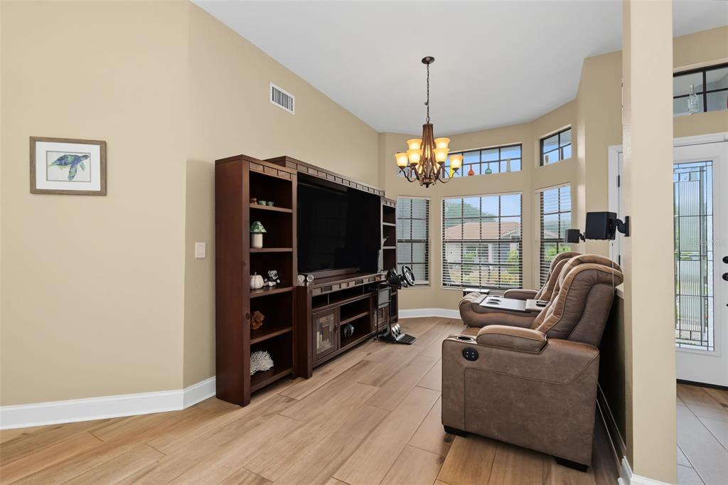 A living room features wood-look tile floors, a large media console, and a brown recliner — 605 TOMOKA DRIVE, PALM HARBOR, FL