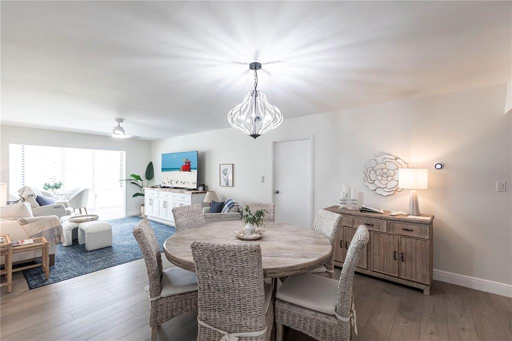 A dining area with a round wooden table and wicker chairs sits before a living room — 1055 W PEPPERTREE DRIVE UNIT 106AA, SARASOTA, FL