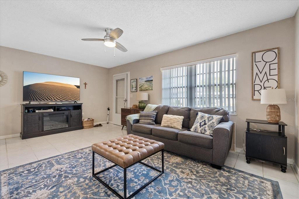 A living room features a gray sofa, a tufted leather ottoman, and a television console — 11635 BAYONET LANE UNIT B, NEW PORT RICHEY, FL