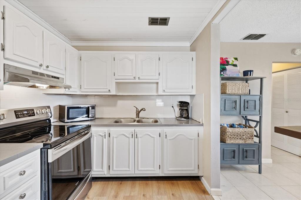 A kitchen features white cabinets, stainless steel appliances, a double sink, and light wood flooring — 11635 BAYONET LANE UNIT B, NEW PORT RICHEY, FL