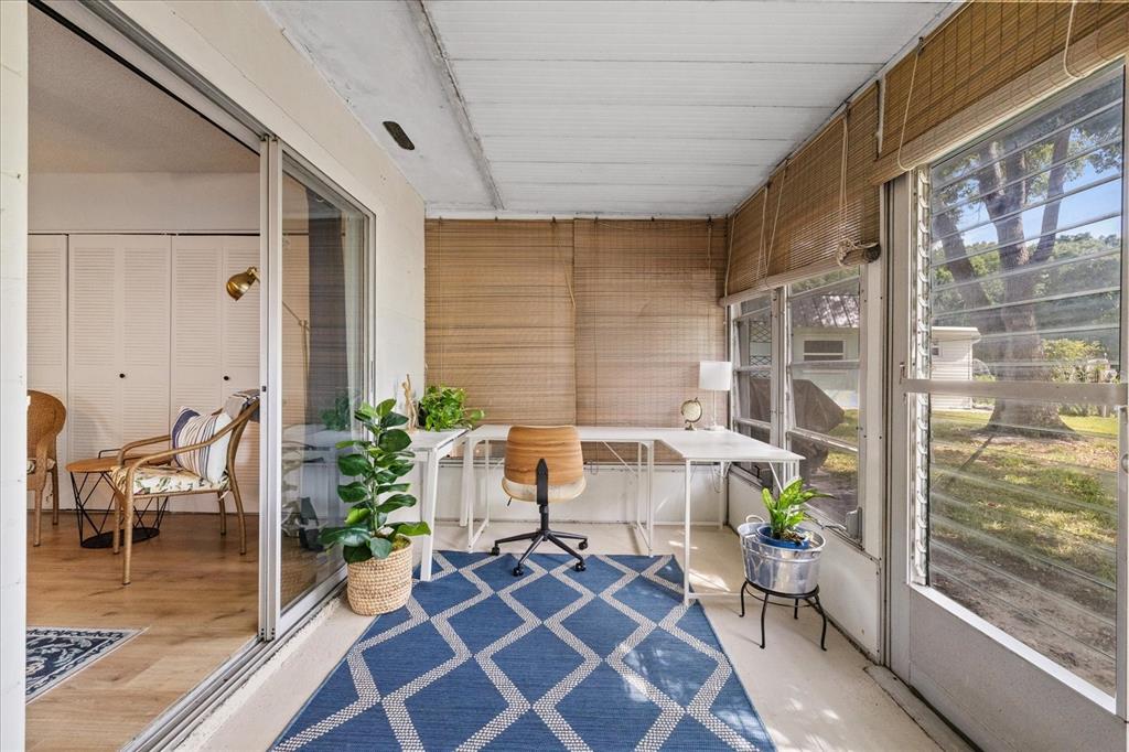 A sunroom features a white L-shaped desk, a blue patterned rug, and bamboo blinds — 11635 BAYONET LANE UNIT B, NEW PORT RICHEY, FL