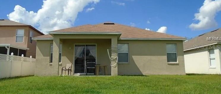 The rear exterior of a tan house features a covered patio, sliding glass doors, and lawn — 2887 PAYNES PRAIRIE CIRCLE, KISSIMMEE, FL