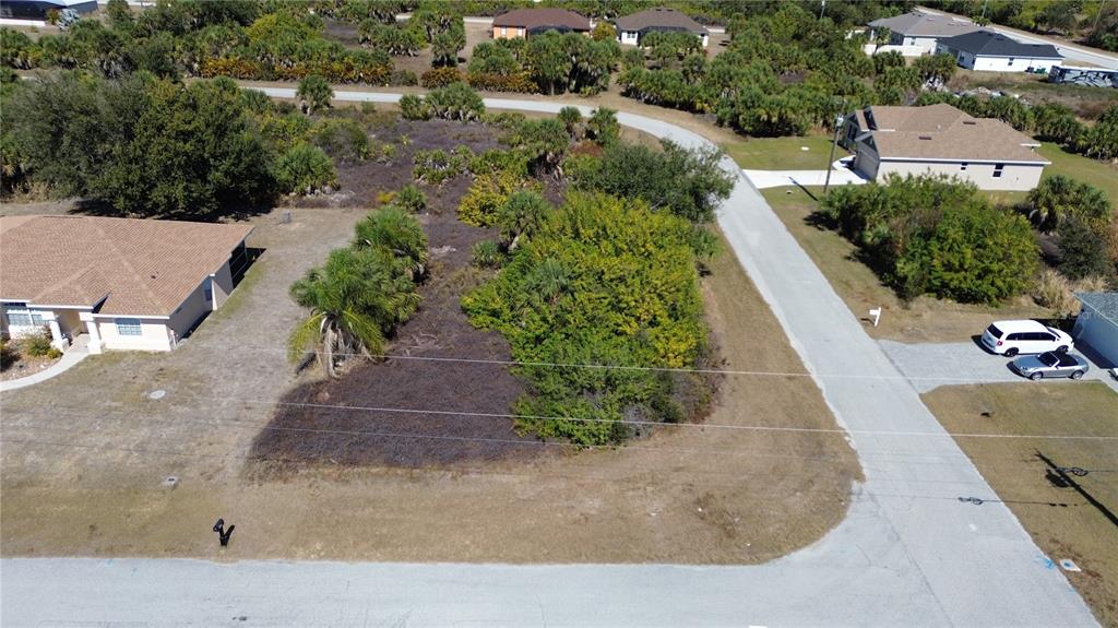 An aerial view shows a vacant, wooded residential lot situated between two houses on a street — 13460 CEDAR CITY AVENUE, PORT CHARLOTTE, FL