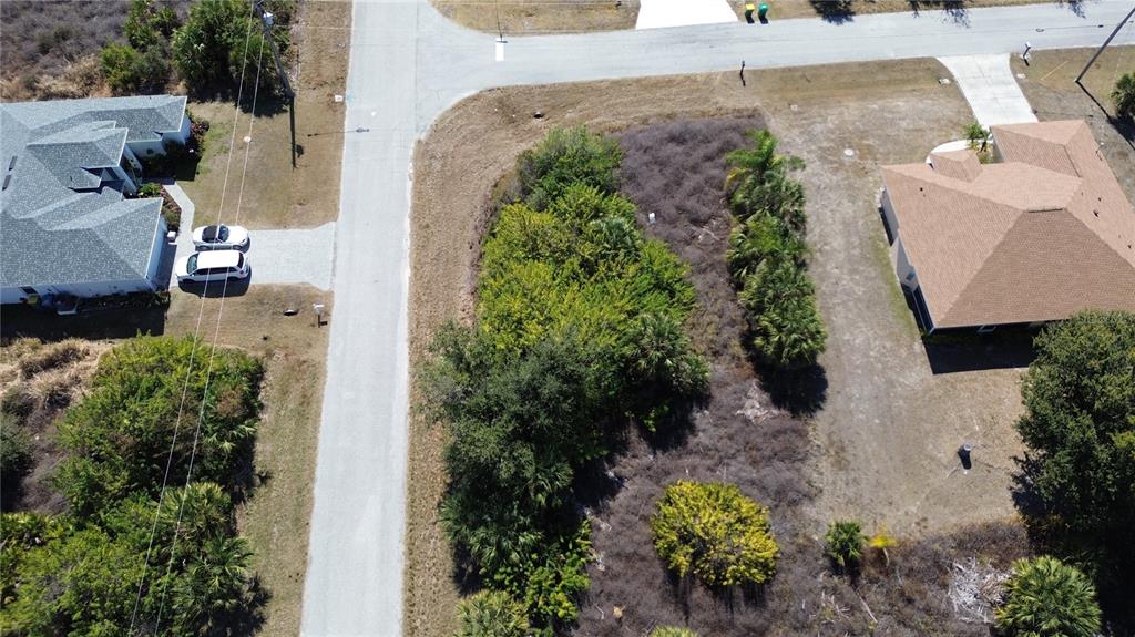 An aerial view shows a vacant, wooded residential lot situated between two houses — 13460 CEDAR CITY AVENUE, PORT CHARLOTTE, FL