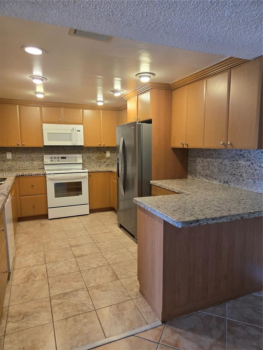 A kitchen features light wood cabinets, granite countertops, tile flooring, and stainless steel appliances — 9735 NW 52nd St # 208, Doral FL 33178, DORAL, FL