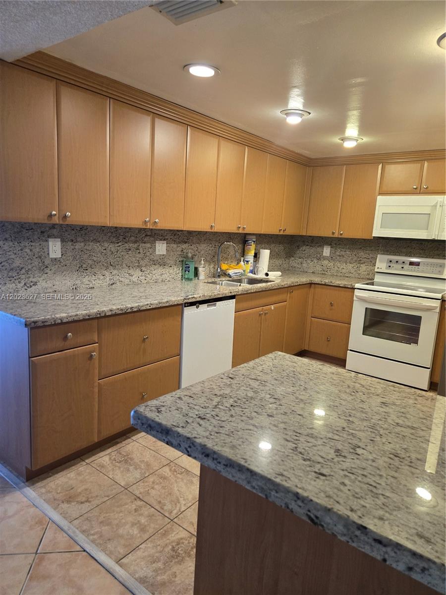 A kitchen features light wood cabinets, granite countertops, and white appliances — 9735 NW 52nd St # 208, Doral FL 33178, DORAL, FL