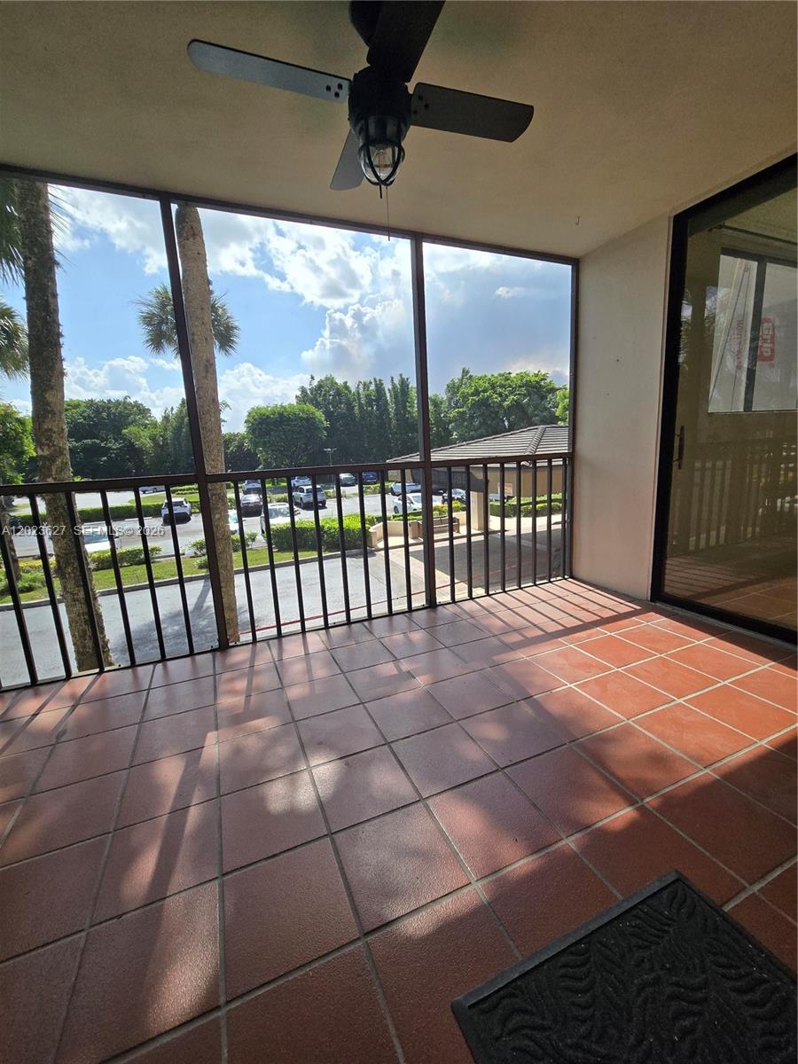 A screened-in balcony features red tile flooring, a ceiling fan, and a view of parking — 9735 NW 52nd St # 208, Doral FL 33178, DORAL, FL