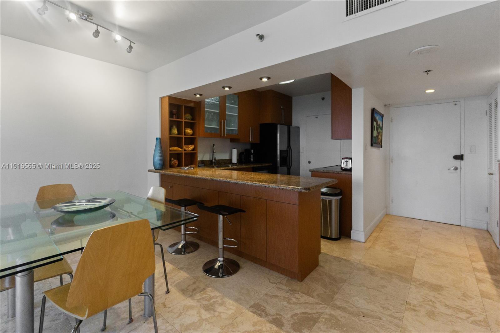 A kitchen with wood cabinets and granite countertops overlooks a dining area with tile floors — 100 Lincoln Rd # 847, Miami Beach FL 33139, MIAMI BEACH, FL