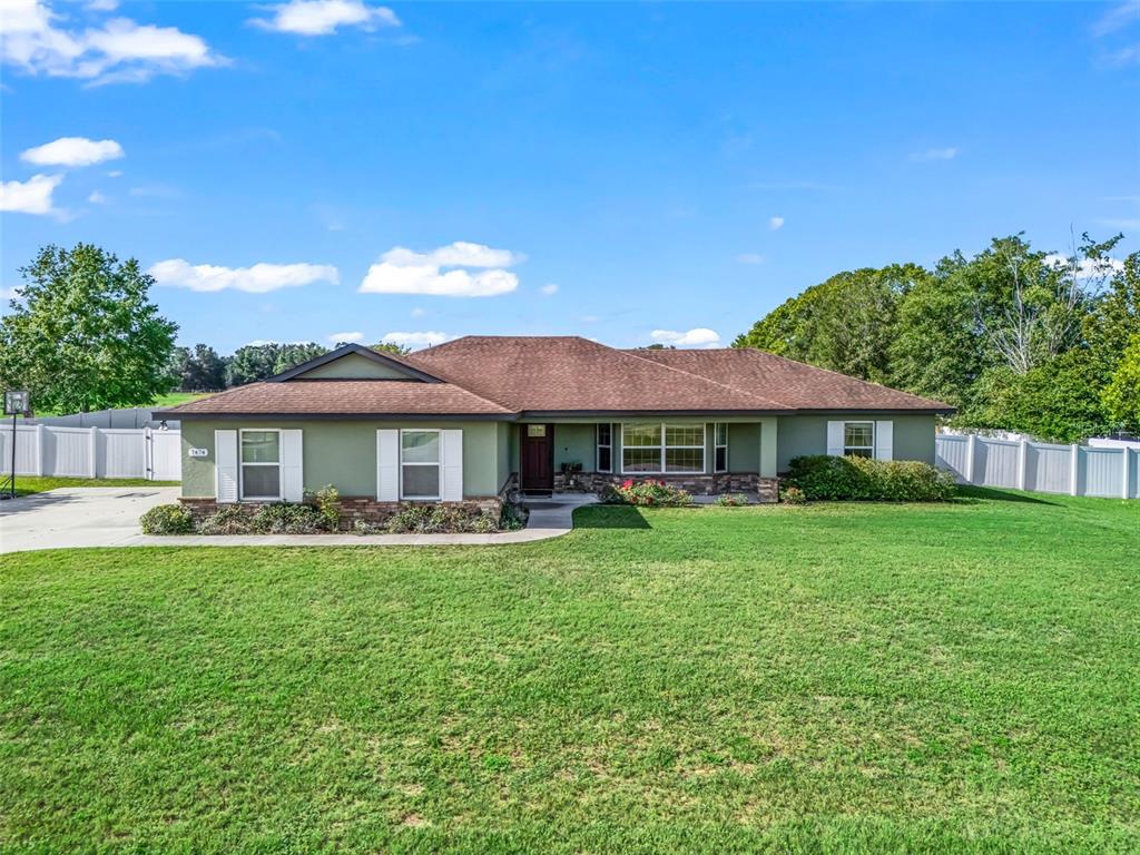A single-story house with green siding, a brown roof, and a large front lawn — 7474 SE 107 PLACE, BELLEVIEW, FL
