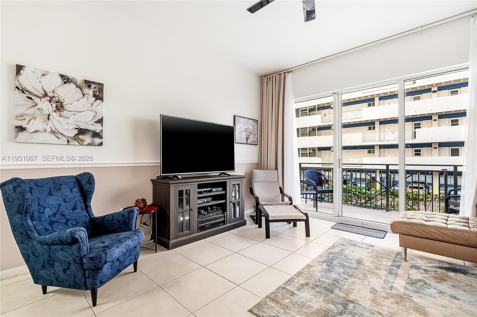 A living room features a blue patterned armchair, a television console, and a balcony view — 2080 S Ocean Dr # 103, Hallandale Beach FL 33009, HALLANDALE BEACH, FL